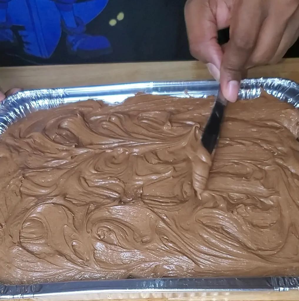 This image depicts moist chocolate cake being frosted with chocolate cream cheese frosting.