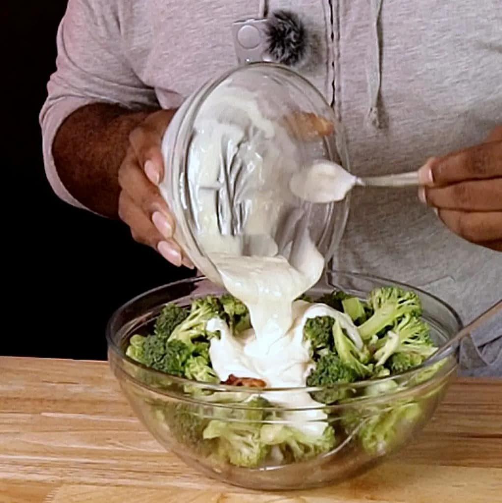 This image depicts Leslie pour creamy dressing over broccoli and other salad ingredients as described by this blog post featured on leslicooks.com.