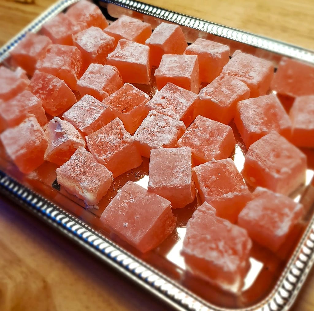 This image show pink cubes of Turkish delight served delicately on a silver serving pan. The image is from a side angle.
