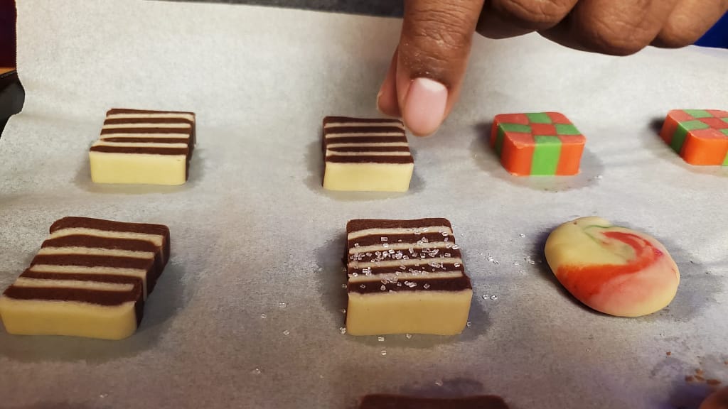 This image depicts the Christmas icebox cookies in a gift box and in a pile on a colling rack. They have checker, stripped, and swirled patterns.