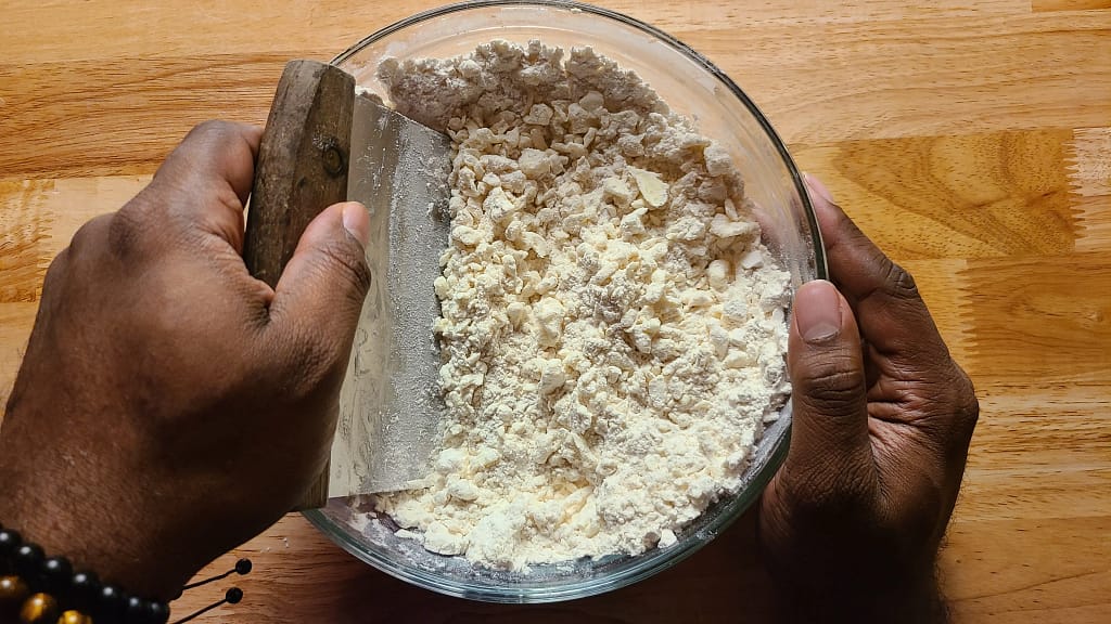 This picture depicts a bowl with ingredients being mixed using a bench scraper