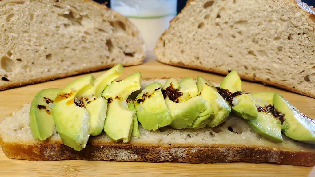 This image depicts sourdough bread with avocado, with hot chili oil and flaky sea salt.