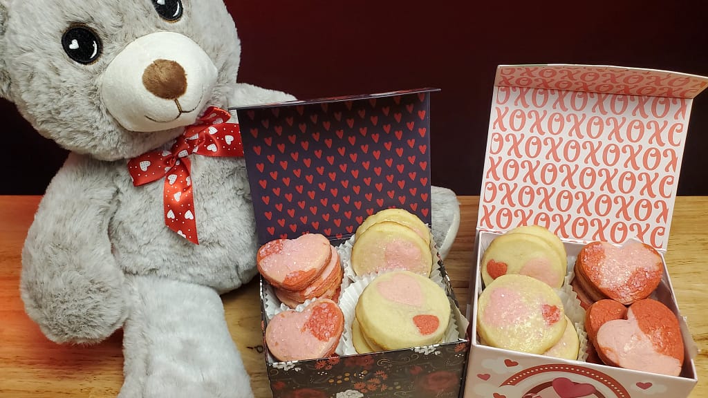 The image depicts a grey teddy bear with the icebox cookies arranged in black and pink decorative gift boxes.