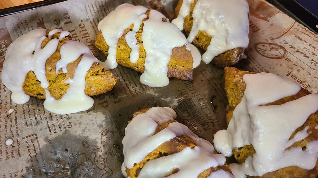 This image depicts pumpkin scones drizzled with maple glaze on a baking sheet with decorative parchment paper.