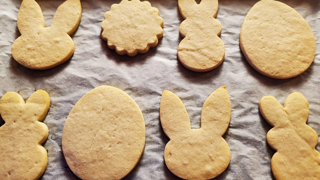 This image of the baked no spread sugar cookies. They have not been iced yet. They on a white parchment paper.