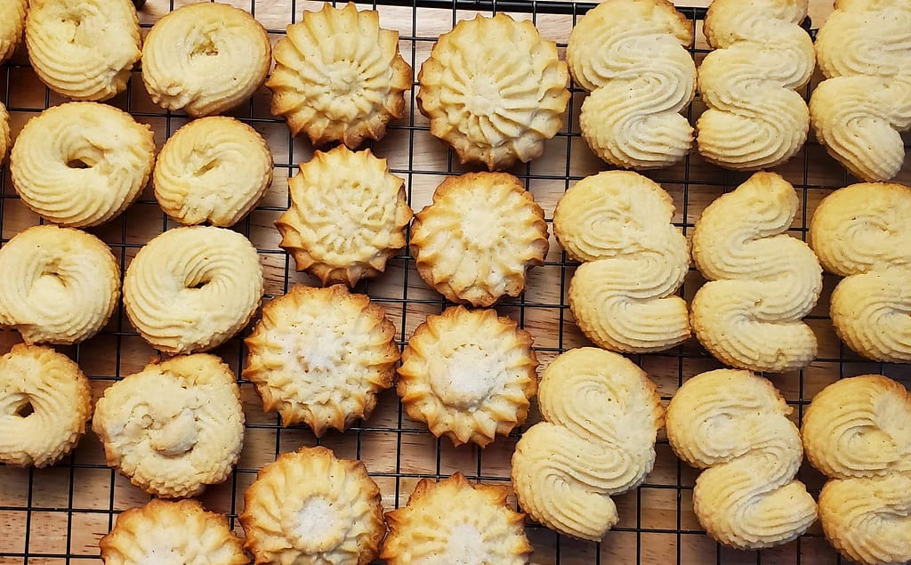 This image depict different shaped Danish Butter Cookies on a cooling rack. They are golden brown.