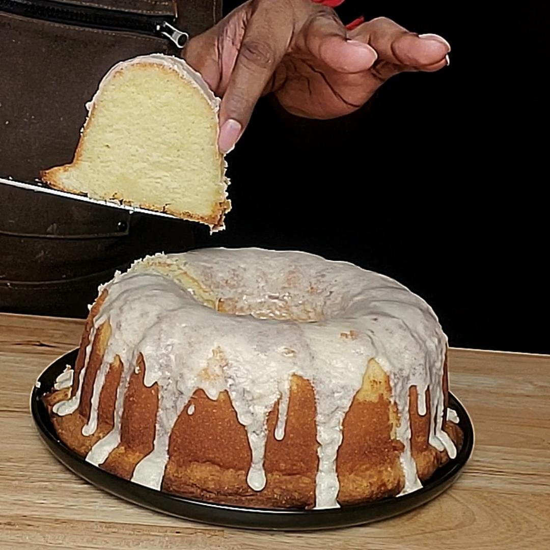 This image depicts 5 flavor pound cake as described by this blog post being sliced. The cake is a nice pale yellow color, The cake is covered with a white Vanilla glaze.