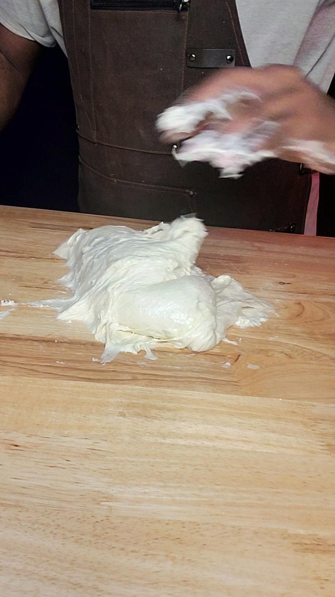 This image depicts Milk Bread dough being kneaded by hand on a wooden countertop.