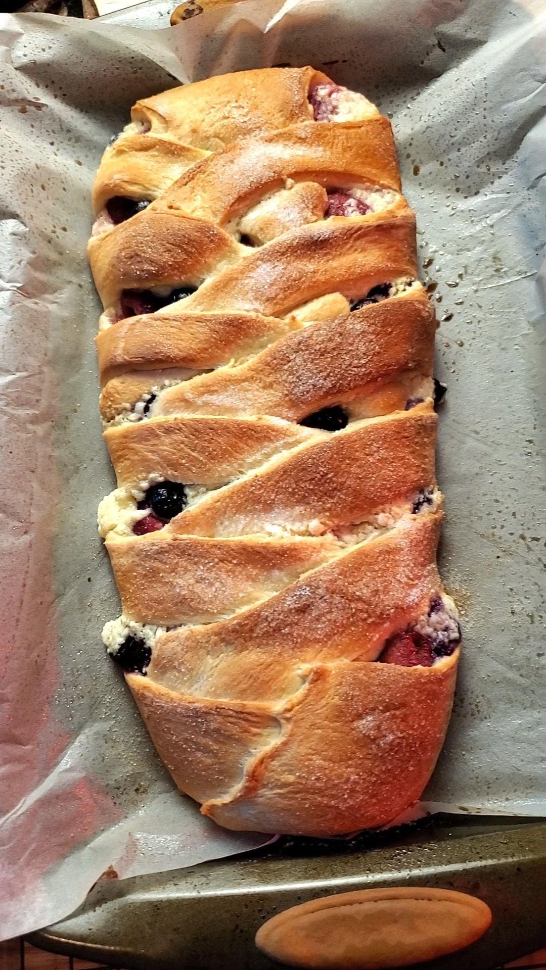 This image depicts a fully baked berry cream cheese braid as described by this recipe blog post on lesliecooks.com. It is golden brown with cream cheese and berries poking through the pastry. This is similar to a cheese Danish.
