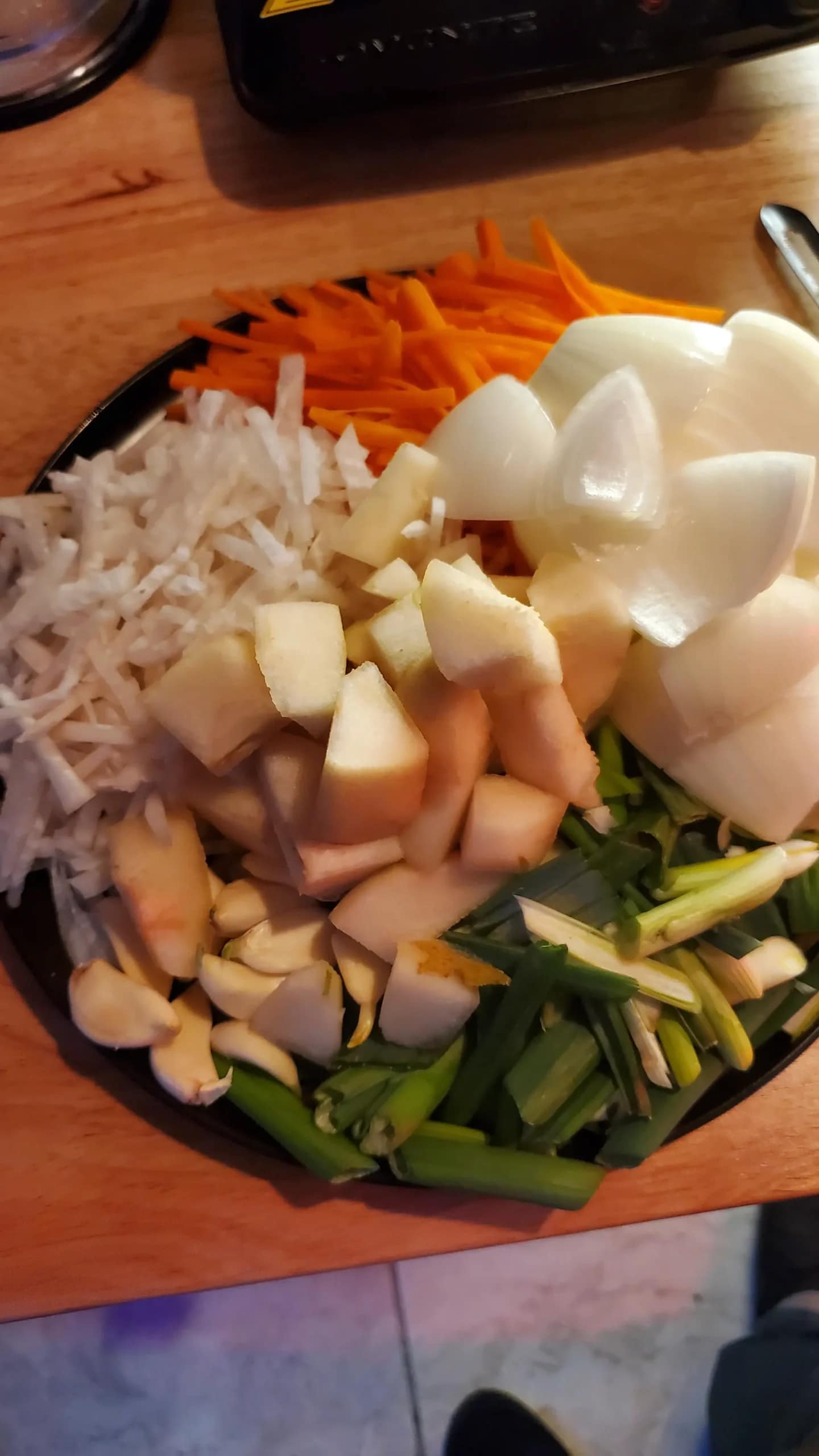 Kimchi Ingredients - Leslie Cooks Game Foodie
Chopped, onions, green onions, carrots, daikon radish, pear, and garlic on a black plate.