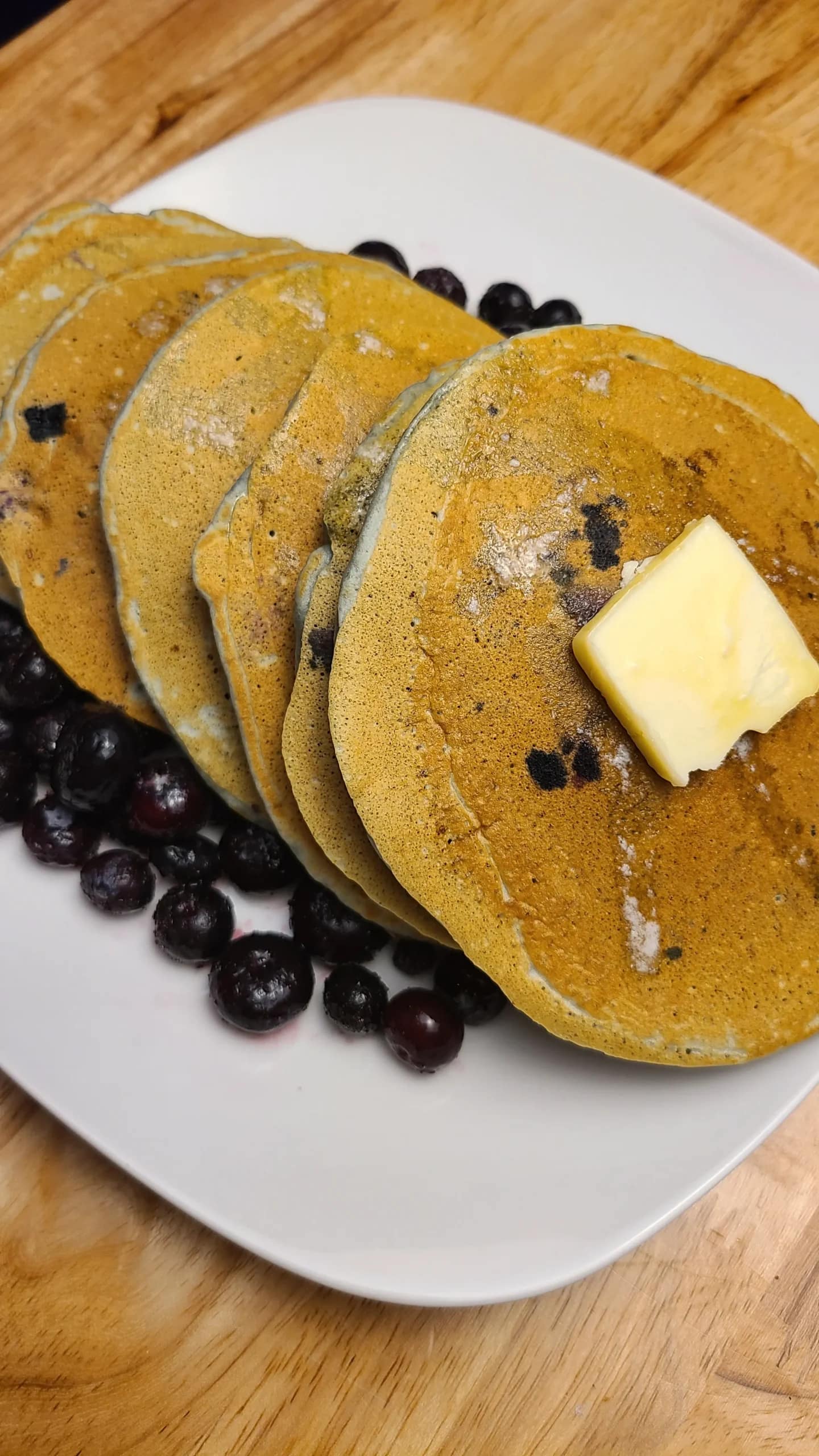 This image depicts Sourdough discard blue berry pancakes on a white plate surrounded by blueberries.