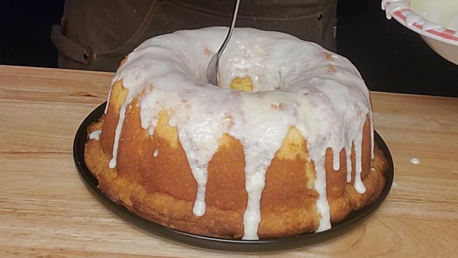 This image depicts 5 flavor pound cake as described by this blog post being sliced. The cake is a nice pale yellow color, The cake is covered with a white Vanilla glaze.