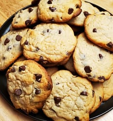 Sour Cream Chocolate chip cookies - leslie cooks. This image depicts golden brown sour cream chocolate chip cookies piled up on a black serving plate. You can see visible chocolate chips in the cookies.