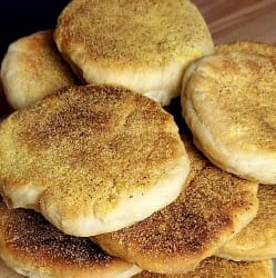 This image depicts english muffins arranged in a stack on a white plate.
