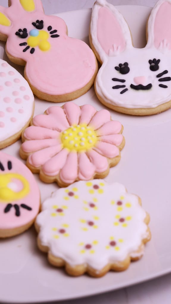This image shows pink and white icing sugar cookies. They are iced using royal icing. There are bunnies and flower cookies. There is one cookie with white pocker dots.