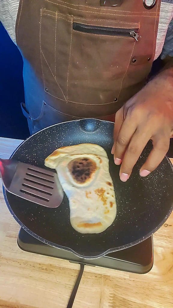 This image depicts naan being cooked in a blue skillet.