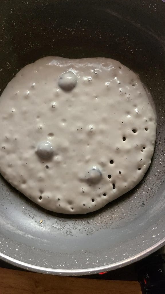 This image depicts a Sourdough discard blueberry pancakes being cooked in a skillet. This sourdough discard recipe is a good way to use up sourdough discard.