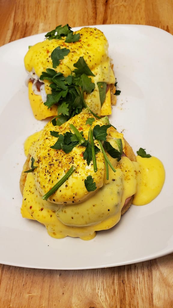 This image shows eggs benedict served on a white plate. Garnished with parsley.