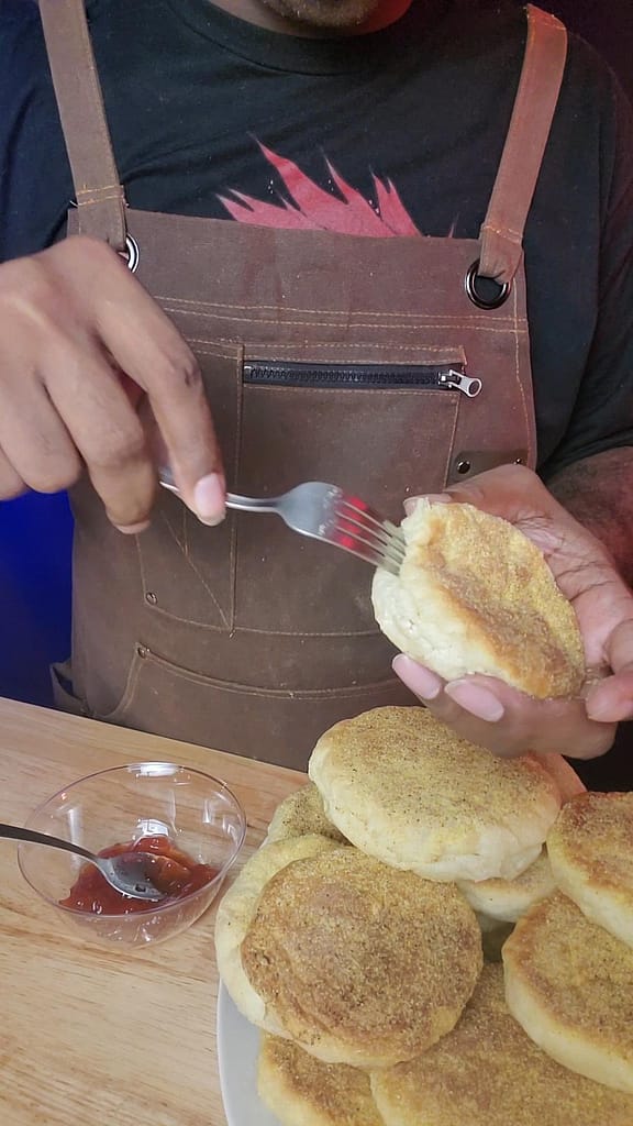 This image shows splitting an english muffin using a fork. There is a pile of english muffins along with some red strawberry jam. These are the result od following the English muffin recipe on this post.