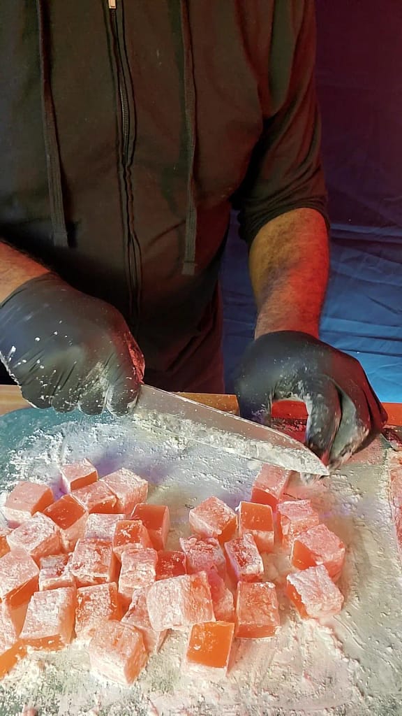 This image depicts cutting of the Turkish delight. Covering each piece in powdered sugar and cornstarch.