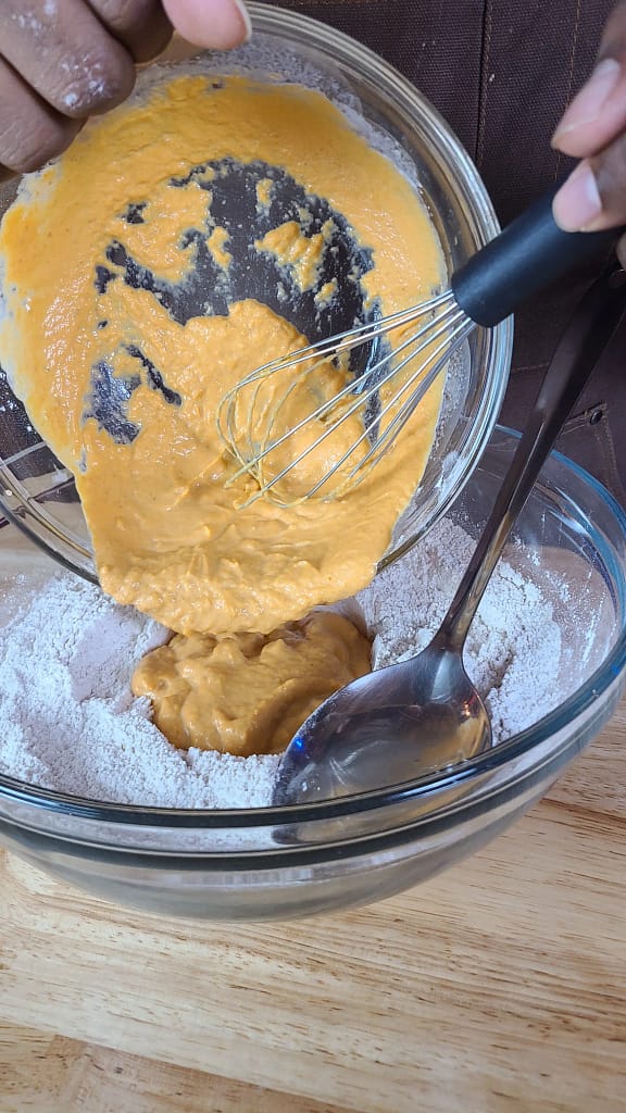 This image depicts wet mixture being added to dry flour mixture. This is a step in the pumpkin scones recipe described on this blog post by lesliecooke.com. The wet mixture is orange and thick.