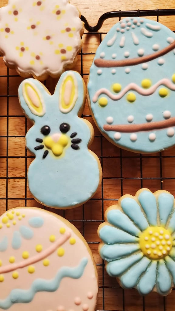 This image show painted sugar cookies as described by this blog post on Lesliecooks.com. There is a white and blue egg design. There is a blue flower, and a white with dotted pattern cookie.