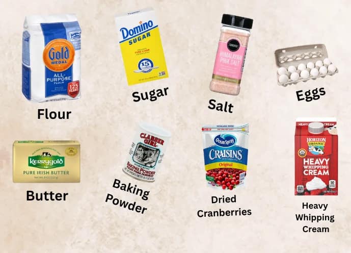 This image show almost all the necessary ingredients needed to make cranberry scones. From left to right- flour, sugar, salt, eggs, butter, baking powder, dried cranberries, and heavy whipping cream.