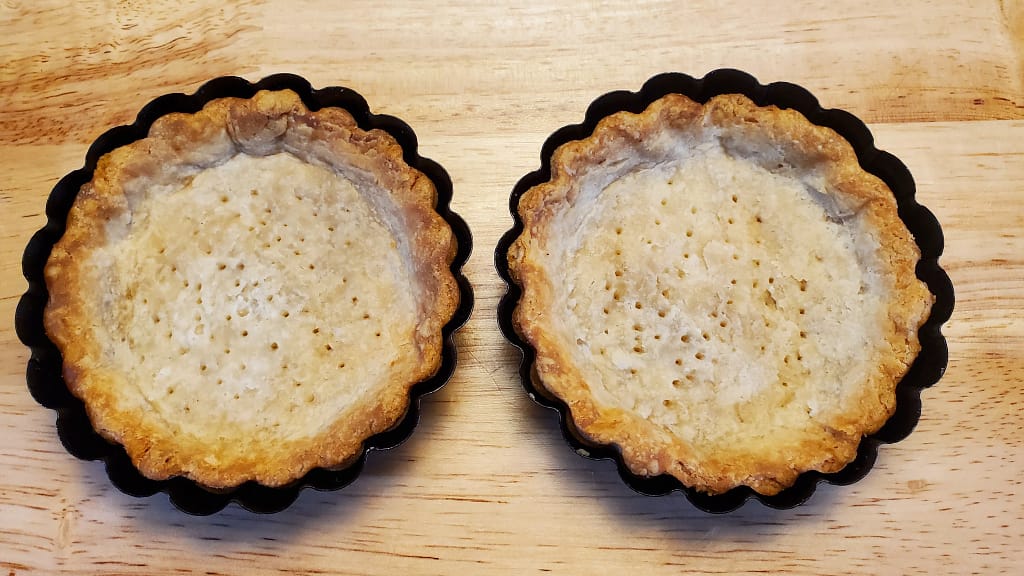 The image depicts two blind baked pie/tart shells. They are golden brown- Leslie Cooks