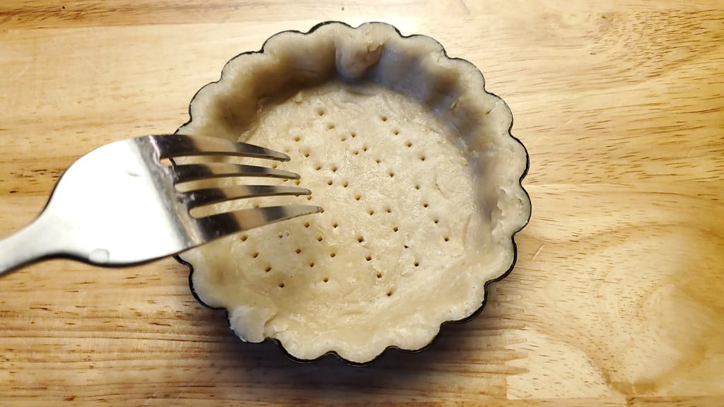 This image depicts a tart crust that has been docked. This means poking little holes at the bottom with a fork or skewer. This helps prevent the bottom of the crust from rising.