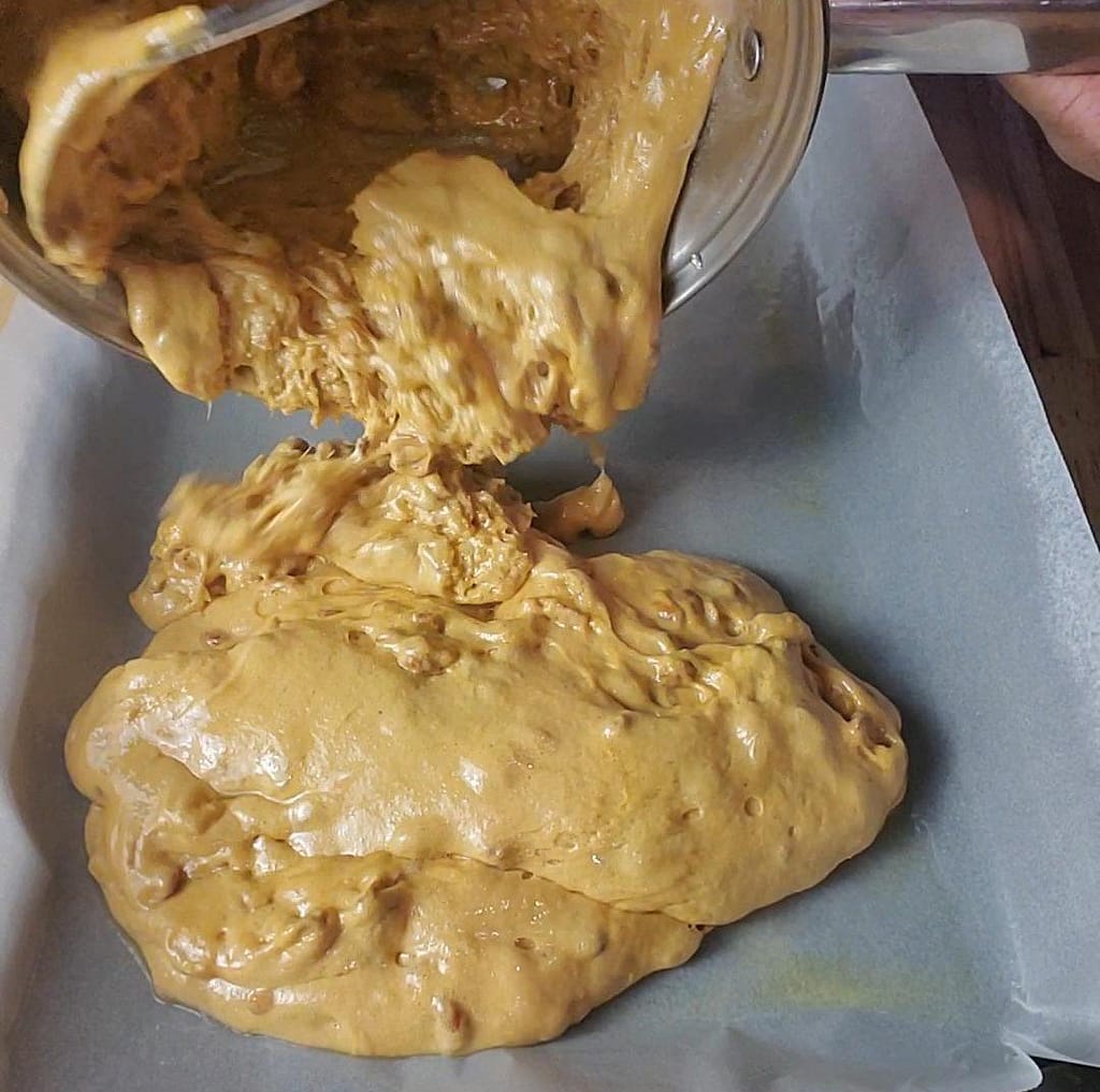 This image depicts hot peanut brittle being pour on a cookie sheet with parchment paper.