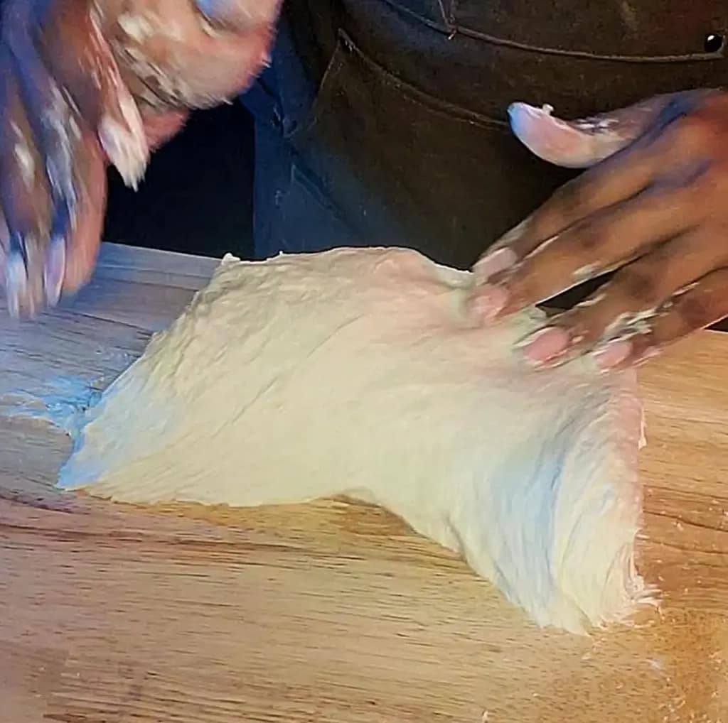 This image depicts naan dough being kneaded on a wooden table.