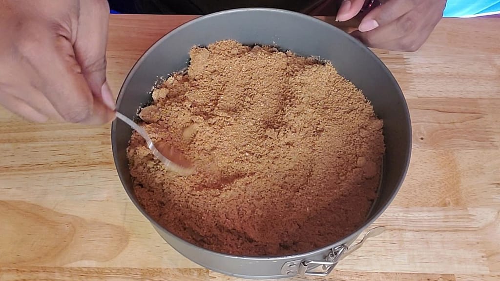 This image depicts spreading graham cracker crumbs into a springform pan.