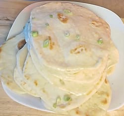 This image depicts the naan bread on a white plate and garnished with chopped green onions. This is the result that following the recipe on this blog post will help to achieve.