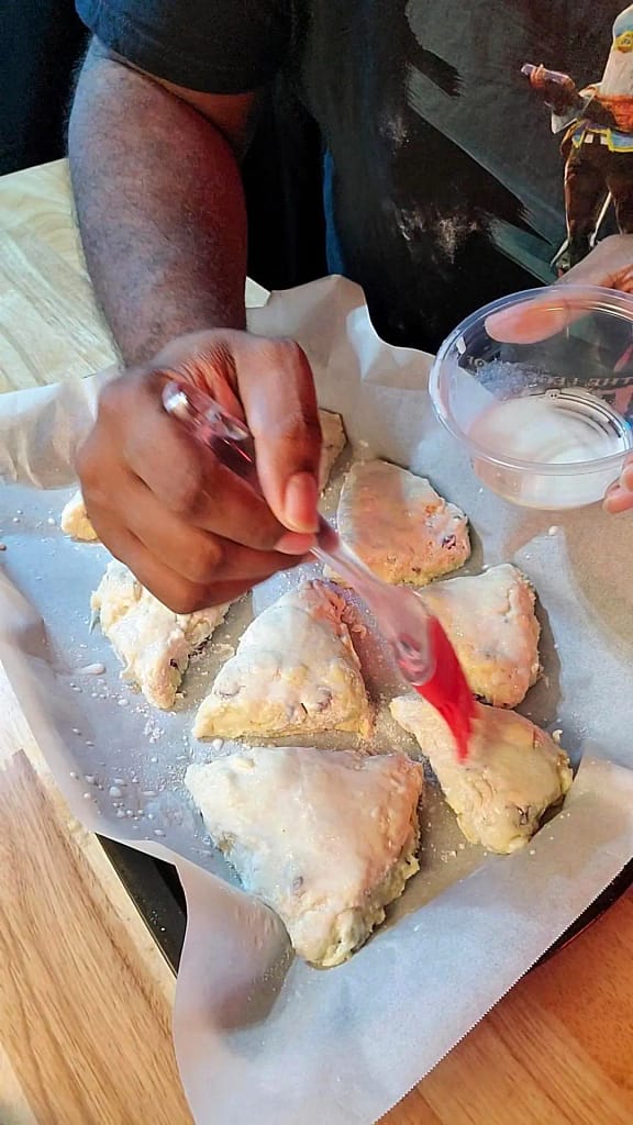 This image depicts cranberry scones being brushed with heavy cream.