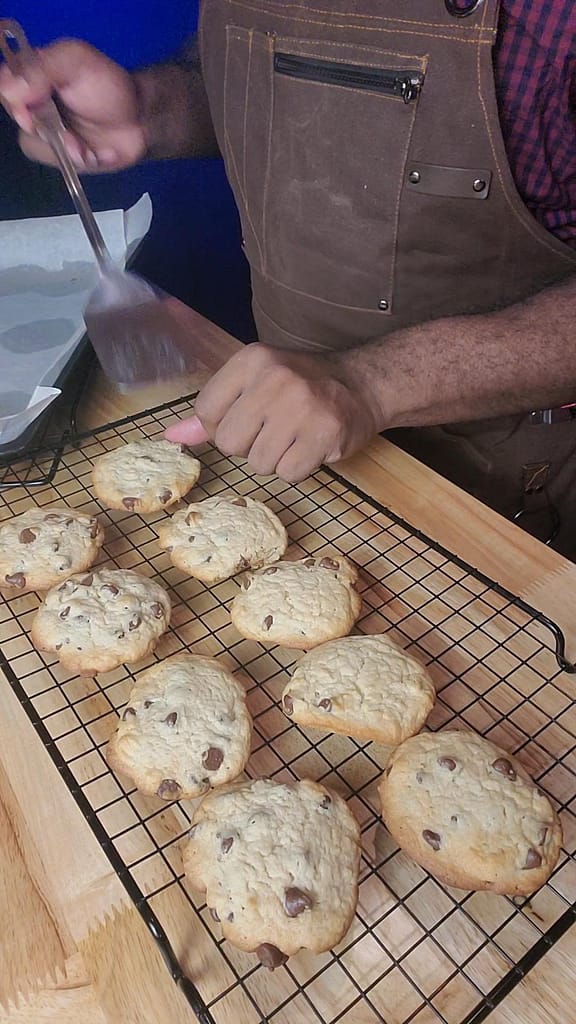 This image depicts Leslie placing the sour cream chocolate chip cookies on a colling rack using a metal spatula.